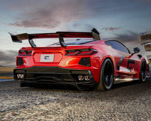 Rear view of a red Chevrolet Corvette C8 ZR1 Stingray with a prominent carbon fiber spoiler against a dynamic sunset backdrop