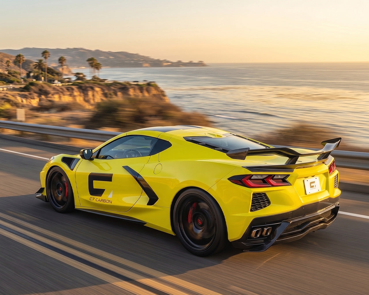 Yellow C8 Corvette Stingray driving along coastline with chassis mounted Z06 style high wing and ducktail lip