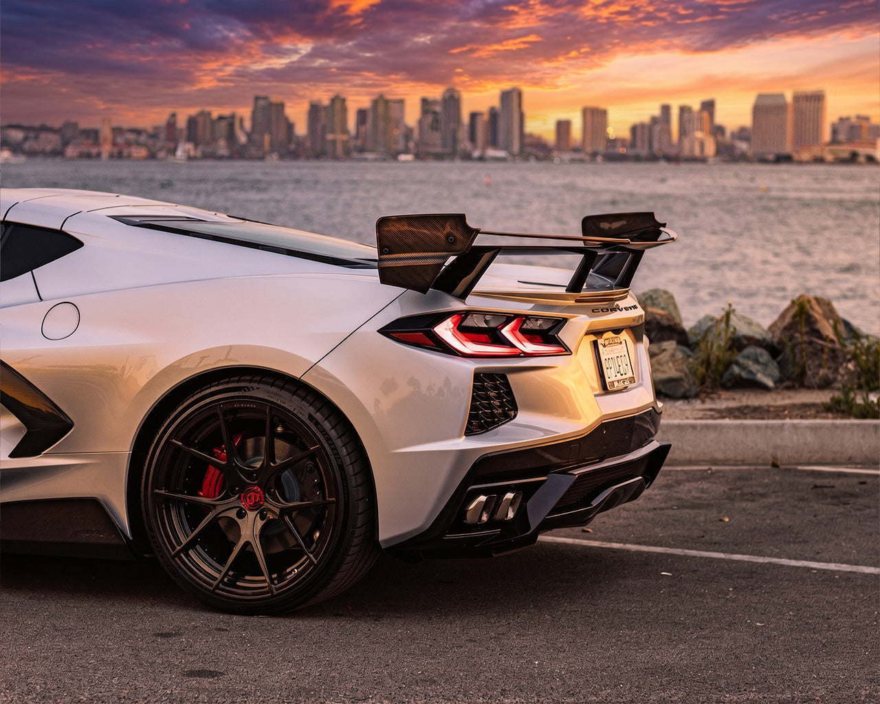 Silver C8 Corvette Stingray with Race Edition carbon fiber rear wing parked in front of city skyline