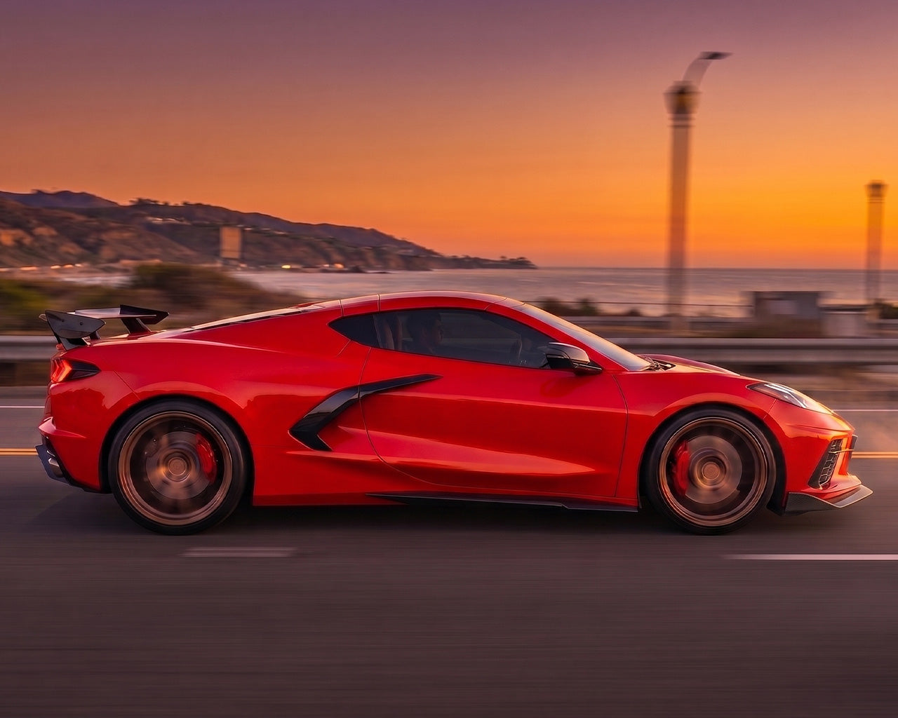 Side profile driving shot of red C8 Corvette Stingray with Z06 style carbon fiber side skirts