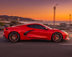 Side profile driving shot of red C8 Corvette Stingray with Z06 style carbon fiber side skirts