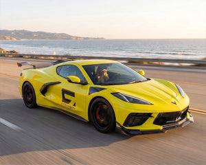 Front angle driving shot of yellow C8 Corvette Stingray on coastal highway with chassis mounted high wing spoiler