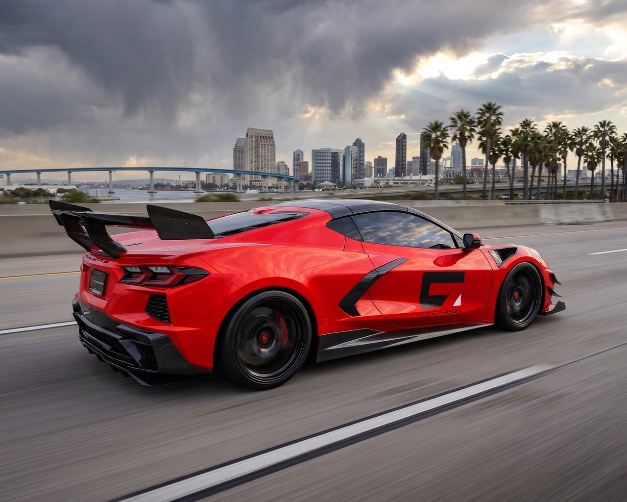 Side angle road view of red C8 Corvette Stingray featuring ZR1 carbon fiber high wing spoiler