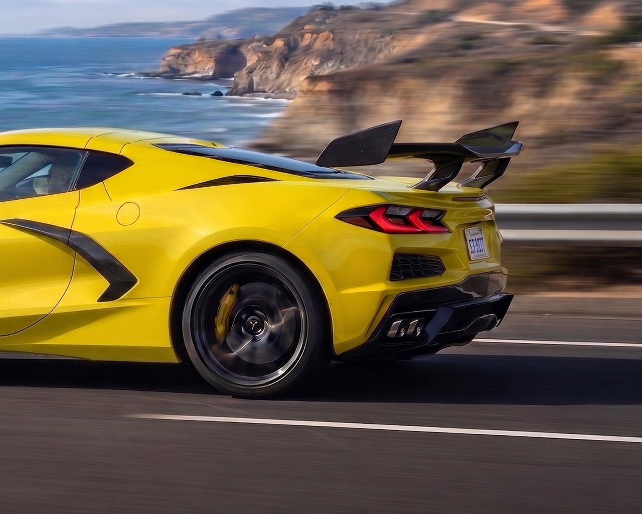 Coastal highway drive view of yellow C8 Corvette with pre-preg carbon fiber ZR1 high wing