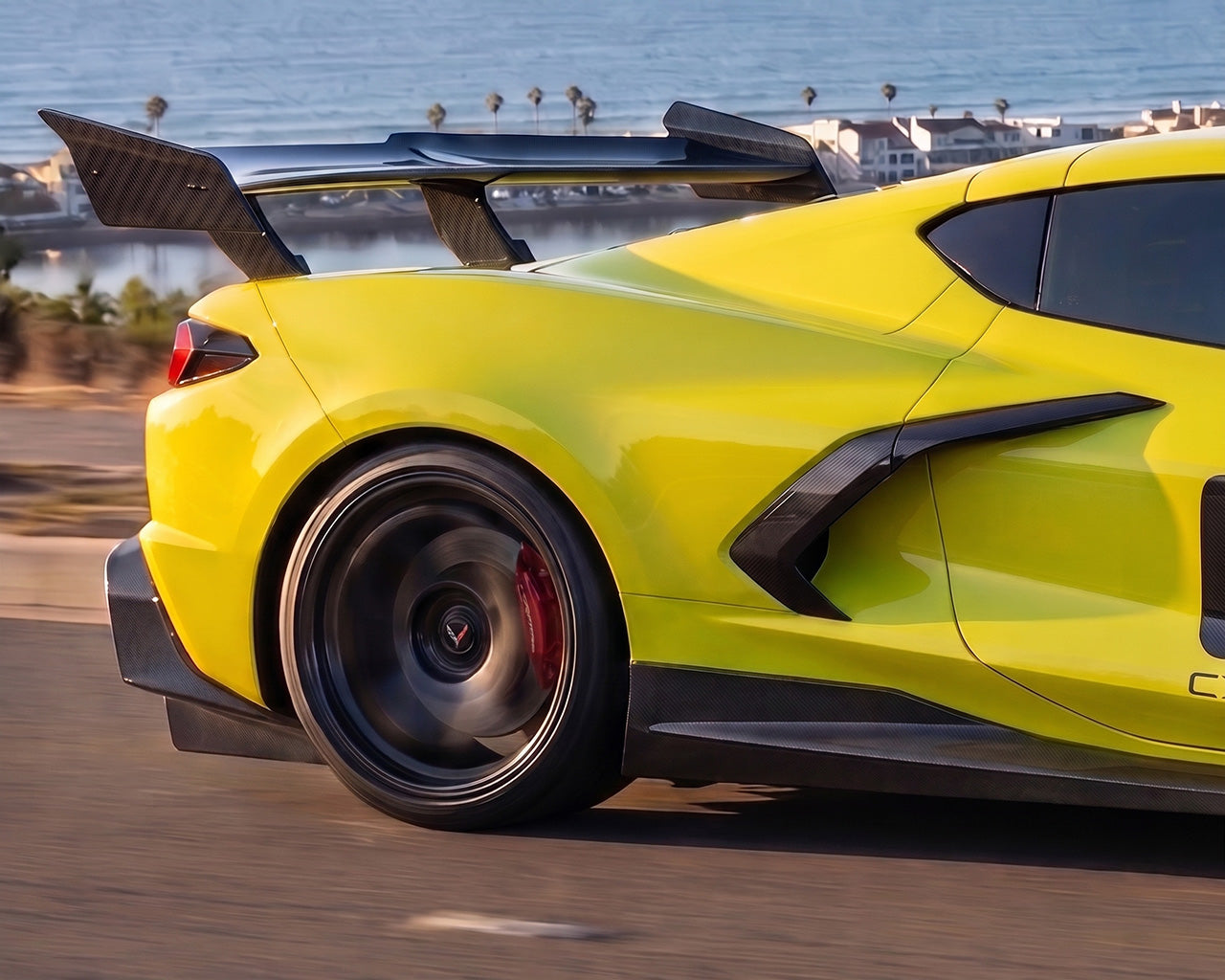 Side profile motion shot of yellow C8 Corvette Stingray with carbon fiber ZR1 style high wing